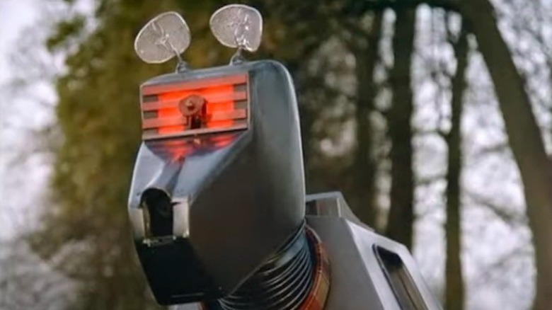 K9 (John Leeson) stands with his eye lit up in a forest in K-9 and Company