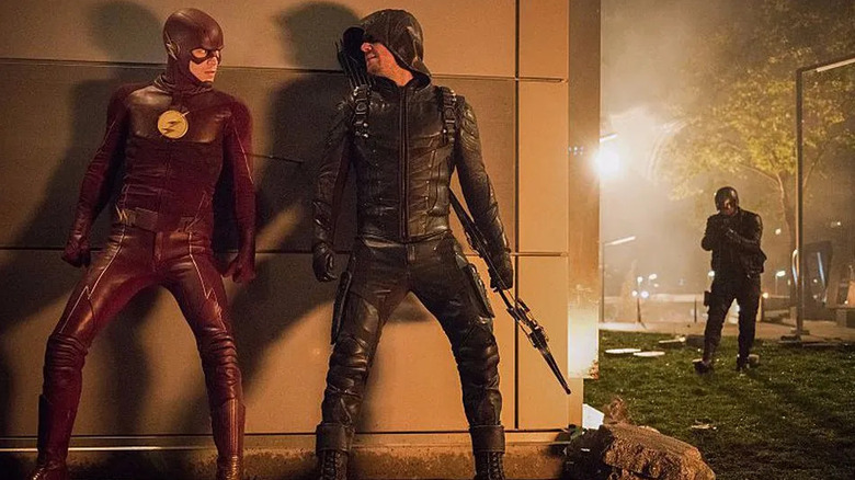 Grant Gustin and Stephen Amell as The Flash and Green Arrow, hiding behind a wall on The Flash