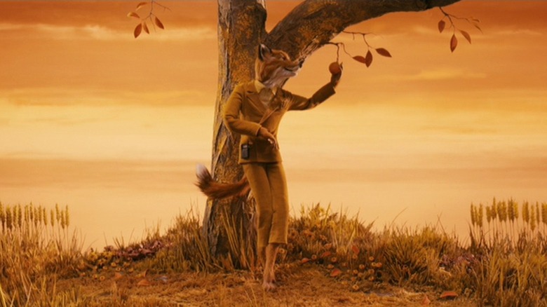 George Clooney as Mr Fox in Fantastic Mr. Fox, standing against a tree surrounded by the autumnal sky, picking fruit from the branches.