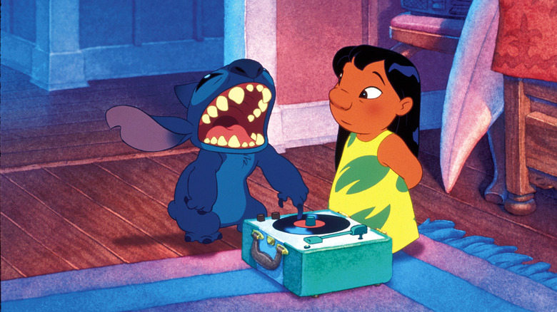 Daveigh Chase as Lilo Pelekai and Chris Sanders as Stitch in Lilo & Stitch, standing next to each other next to a tiny record player while Stitch scratches the vinyl with his claw.
