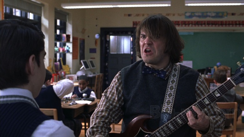 Jack Black as Dewey Finn in School of Rock, making an expressive grimace on his face while he wields a guitar in the classroom.