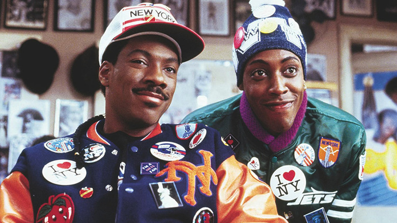 Akeem Joffer (Eddie Murphy) and Semmi (Arsenio Hall) smile wearing sports jackets loaded with patches and buttons in Coming to America