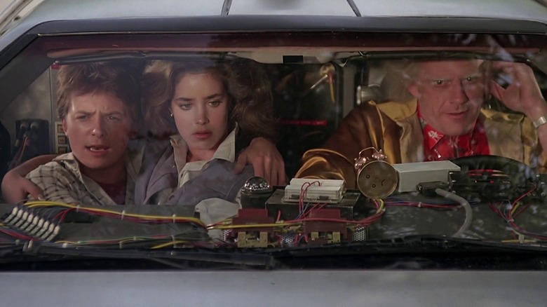 Marty McFly (Michael J. Fox), Jennifer Parker (Claudia Wells), and Doc Brown (Christopher Lloyd) crowd into a DeLorean in Back to the Future