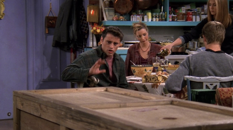 Matt LeBlanc as Joey Tribbiani talking to a box while Jennifer Aniston as Rachel Green pours Lisa Kudrow as Phoebe Buffay wine in the Friends episode "The One with Chandler in a Box"