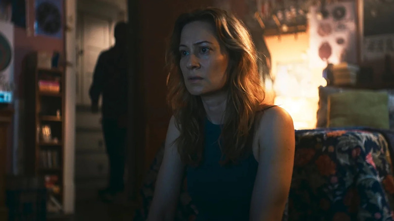 Camille Sullivan as Mia watching a TV while a figure lurks in the background in Shelby Oaks