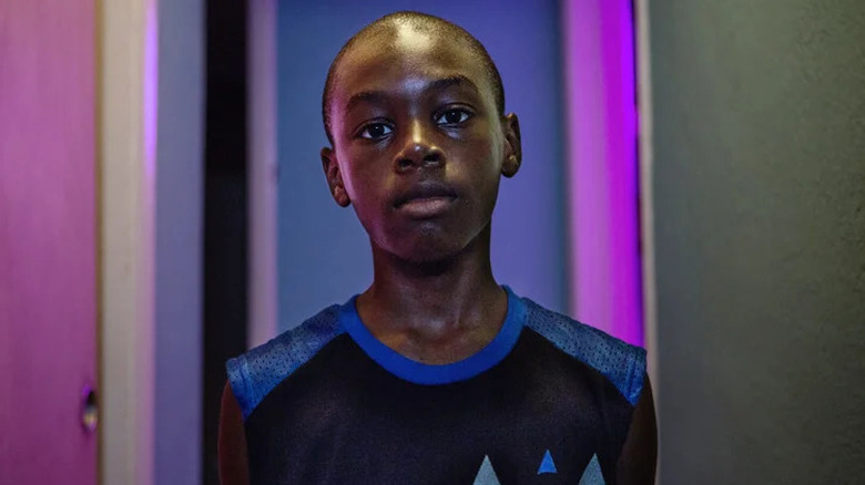 Alex Hibbert as Chiron looking straight ahead with pink light in the background in Moonlight