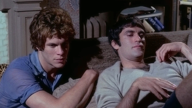 Robert La Tourneaux as Cowboy Tex kneeling next to Cliff Gorman as Emory on the couch in The Boys in the Band