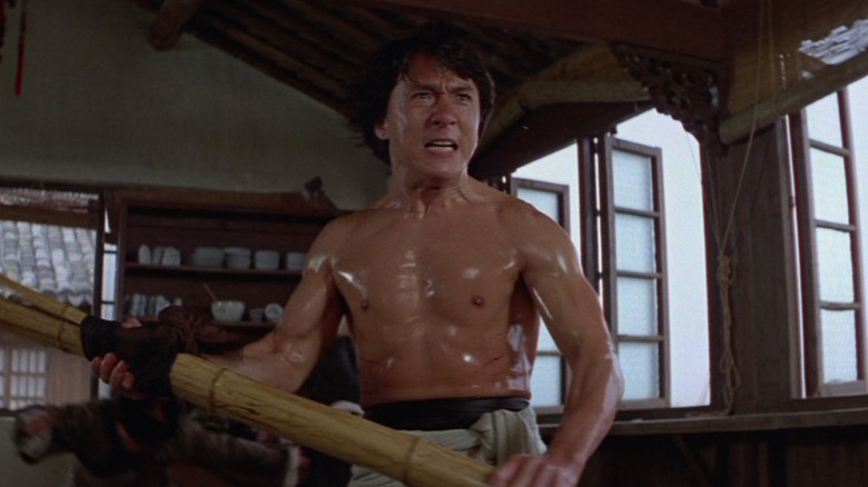 Wong Fei-hung (Jackie Chan) stands topless holding a bamboo pole in Drunken Master II