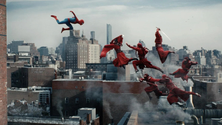 Tom Holland as Peter Parker/Spider-Man, diving through the air toward the Red Hand fighters that are jumping up toward him.