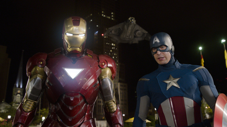 Robert Downey Jr. as Tony Stark/Iron Man and Chris Evans as Steve Rogers/Captain America in The Avengers, standing next to each other in costume at night in front of a tall building and flying ship.
