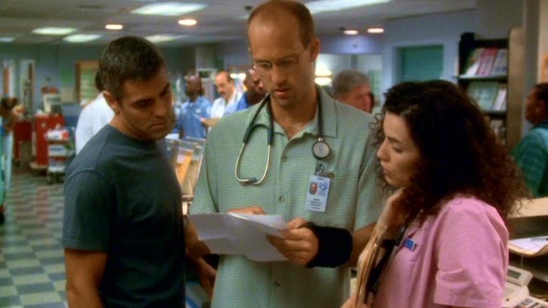 George Clooney as Dr. Doug Ross, Anthony Edwards as Dr. Mark Greene, and Julianna Margulies as Carol Hathaway looking at papers on ER