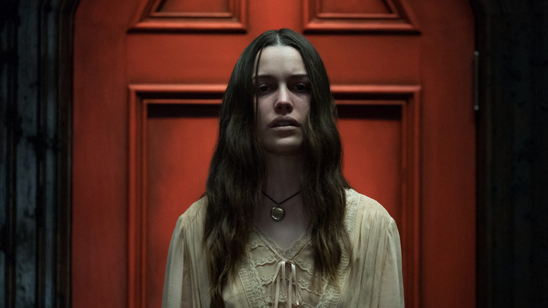 A ghostly Nell Crain (Victoria Pedretti) stands before a red door in The Haunting of Hill House