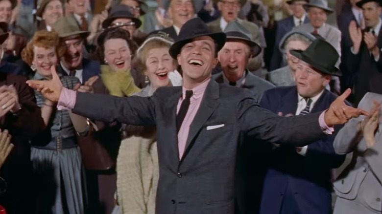 Gene Kelly as Ted Riley in It's Always Fair Weather, throwing out his arms wide in front of a cheering crowd