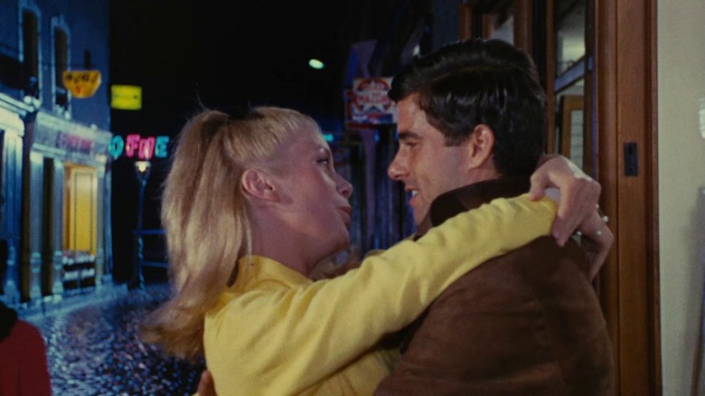 Catherine Deneuve as Geneviève and Nino Castelnuovo as Guy embrace on a blue-lit street in The Umbrellas of Cherbourg