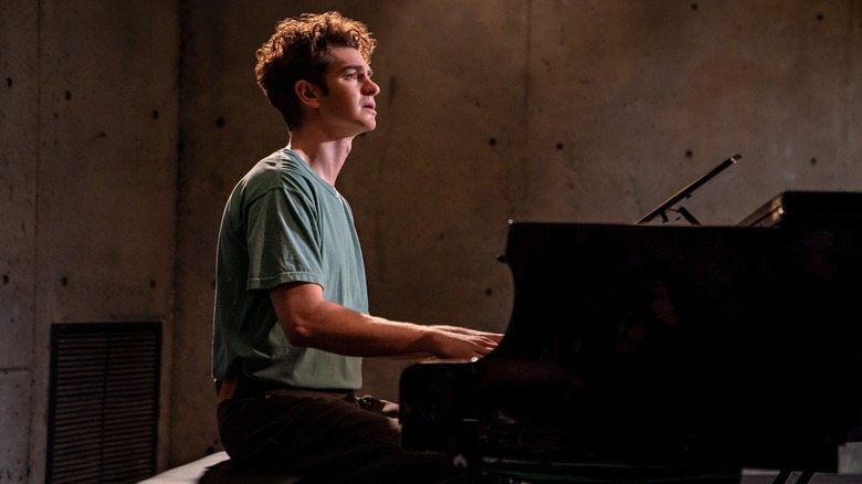 Andrew Garfield as Jonathan Larson sits at a piano looking distraught