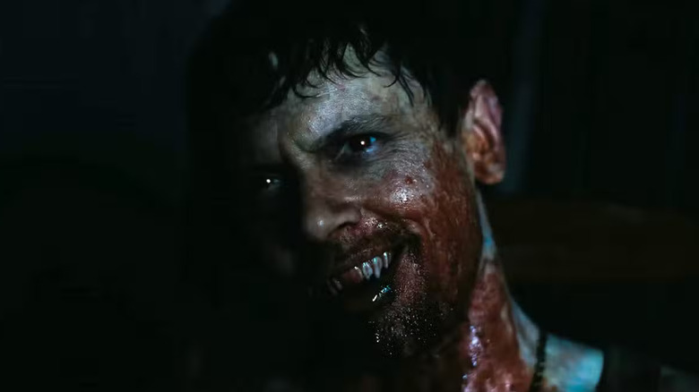 Jack O'Connell as Remmick in Sinners, face bloodied, fangs out, looking off in the distance.