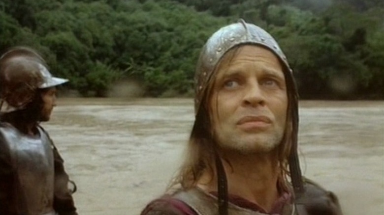 Klaus Kinski as Lope de Aguirre standing next to river and looking at sky with another man behind him in Aguirre, the Wrath of God