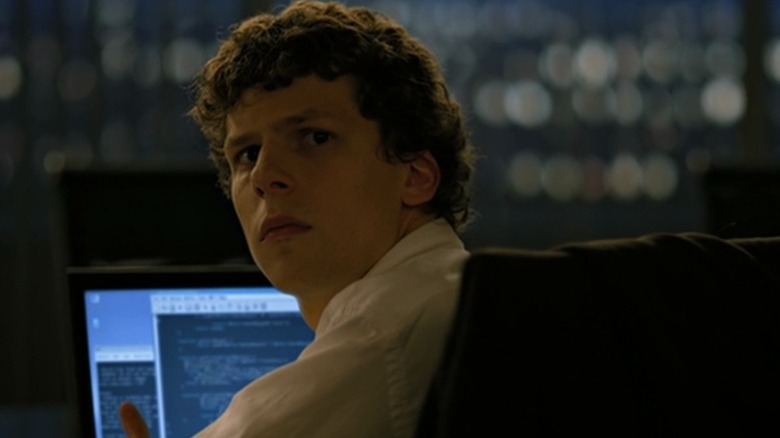 Jesse Eisenberg as Mark Zuckerberg sitting at computer desk and looking back over shoulder in The Social Network