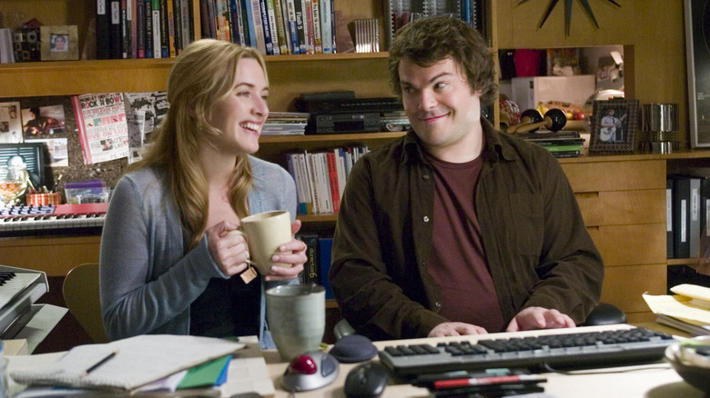 Kate Winslet as Iris smiling with a cup of tea next to Jack Black as Miles smiling with hands on keyboard in The Holiday