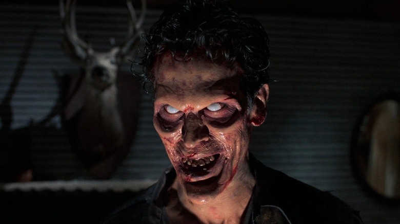 Bruce Campbell as Evil Ash Williams in Evil Dead II, looking menacingly past the camera with his bloodied, hallowed out face and white eyes.