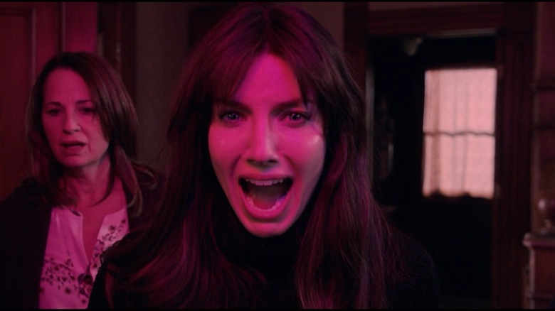 Annabelle Wallis as Madison Mitchell and Paula Marshall as Beverly in Malignant, both bathed in a magenta light with the former screaming at something out of frame.