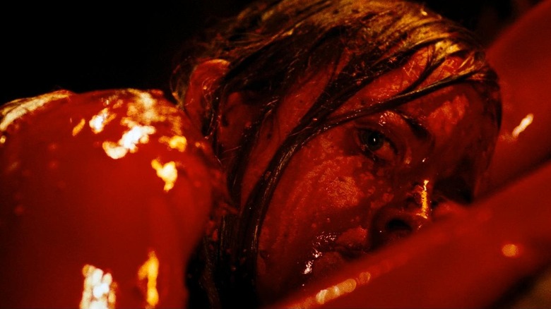 Shauna Macdonald as Sarah in The Descent, laying stomach-down covered in blood and looking past the camera.