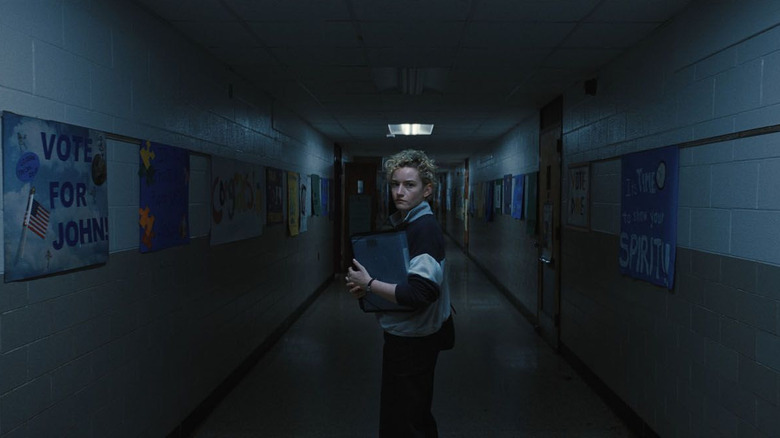 Julia Garner as Justine in Weapons, standing in the dark in an abandoned school hallway.