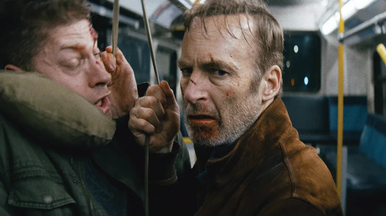 Hutch Mansell (Bob Odenkirk) looks forward while restraining a man with a strap in a bus in Nobody