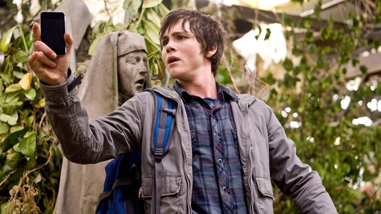 A distraught Percy Jackson (Logan Lerman) check his phone by a stone statue in Percy Jackson & the Olympians: The Lightning Thief