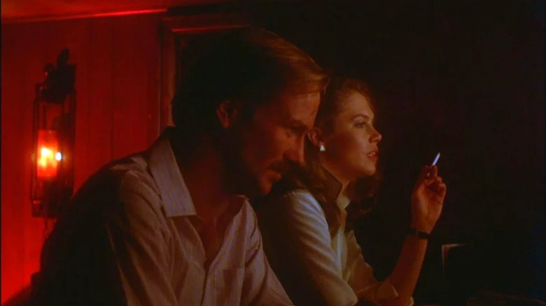 William Hurt as Ned standing next to Kathleen Turner as Matty smoking a cigarette in red light in Body Heat