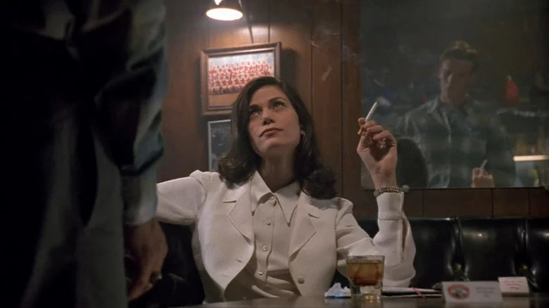 Linda Fiorentino as Bridget sitting in bar wearing white suit and smoking while looking up at a man in The Last Seduction