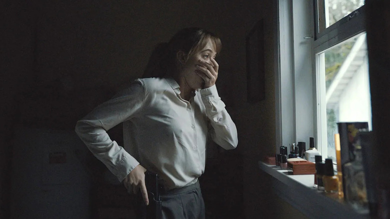Maika Monroe as Lee Harker, covering her mouth looking out of a window in Longlegs