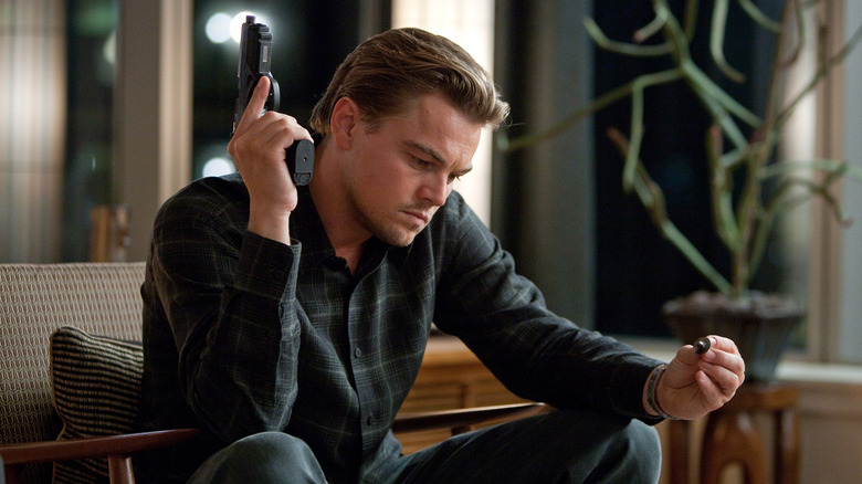 Leonardo DiCaprio as Cobb, holding a gun and examining his top in Inception