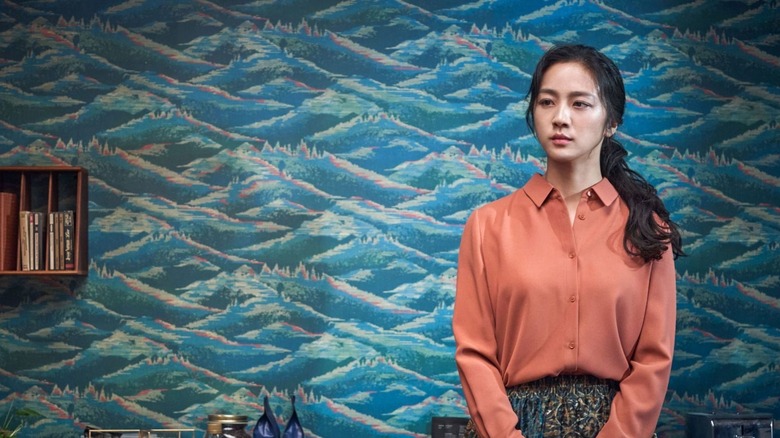 Song Seo-rae (Tang Wei) stands before a wall with ornate wallpaper in Decision to Leave