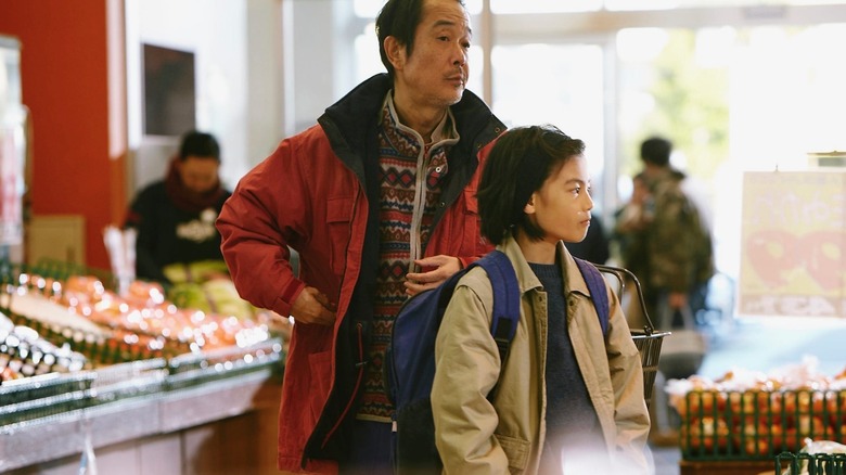 Osamu Shibata (Lily Franky) stuffs his coat pockets at a supermarket by Yuri (Miyu Sasaki) in Shoplifters
