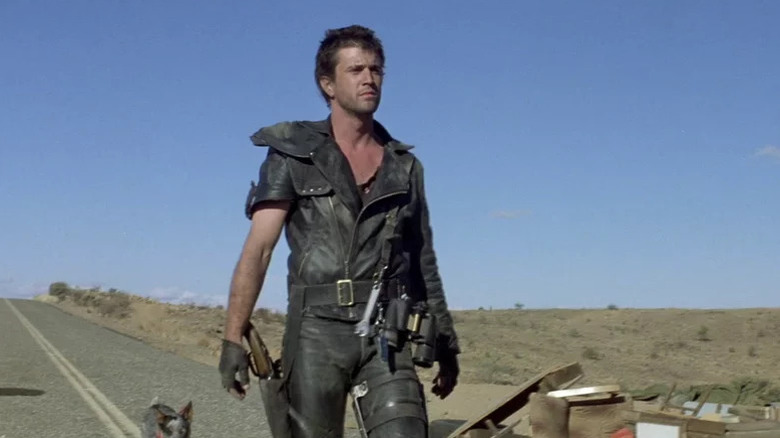 Max Rockatansky (Mel Gibson) stands by wreckage on a desolate road in Mad Max 2: The Road Warrior