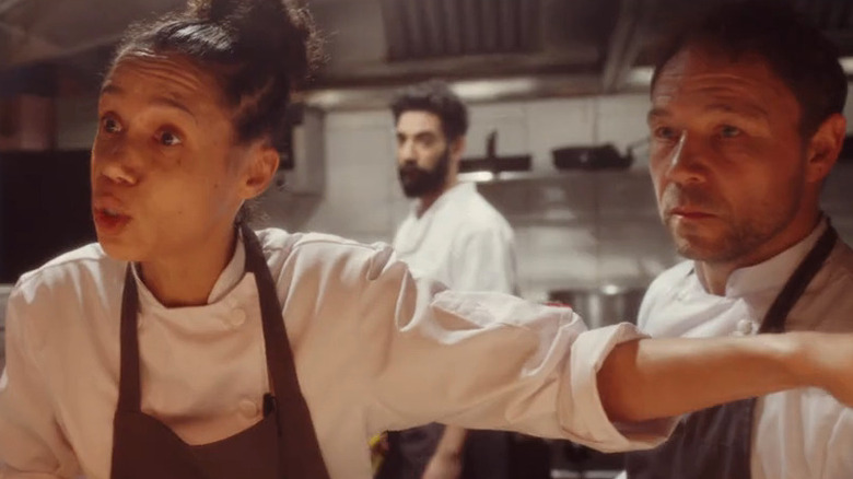 Vinette Robinson as Carly pointing arm and speaking, Stephen Graham as Andy next to her, Ray Panthaki as Freeman in the background, in restaurant kitchen with chef's coats in Boiling Point
