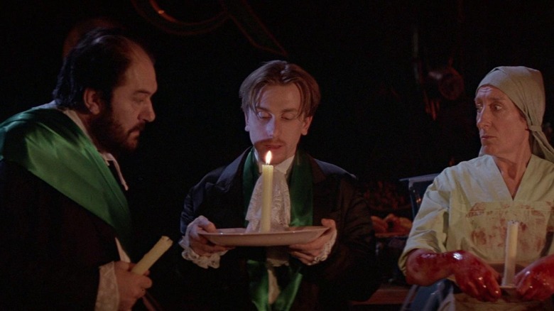 Michael Gambon as Albert in suit and green sash, Tim Roth as Mitchel in similar outfit holding plate with candle, Janet Henfry as Alice in maid outfit with bloody hands and candle in The Cook, the Thief, His Wife & Her Lover