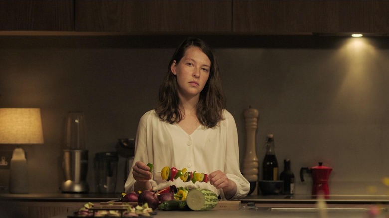 Annes Elwy as Cadi standing in kitchen holding skewer of vegetables in The Feast