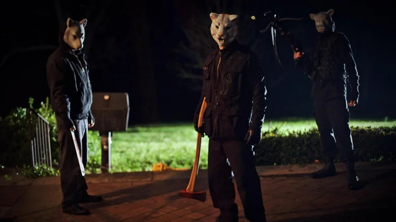 Three figures dressed in black wearing animal masks and holding weapons in You're Next