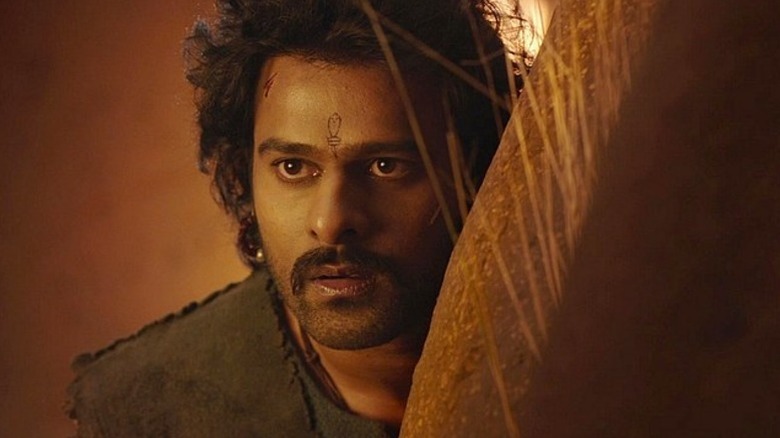 Prabhas as Sivudu hides behind a large stone in Baahubali: The Beginning