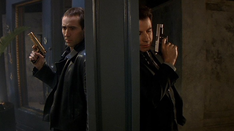 Nicolas Cage and John Travolta as Castor Troy and Sean Archer wielding guns while leaning on opposite sides of the same wall in Face/Off