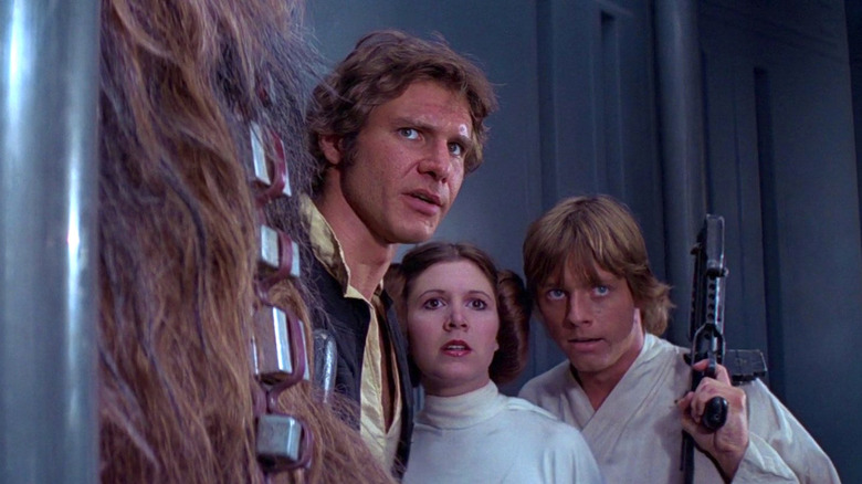 Peter Mayhew as Chewbacca, Harrison Ford as Han Solo, Carrie Fisher as Princess Leia, and Mark Hamill as Luke Skywalker stand side by side in Star Wars