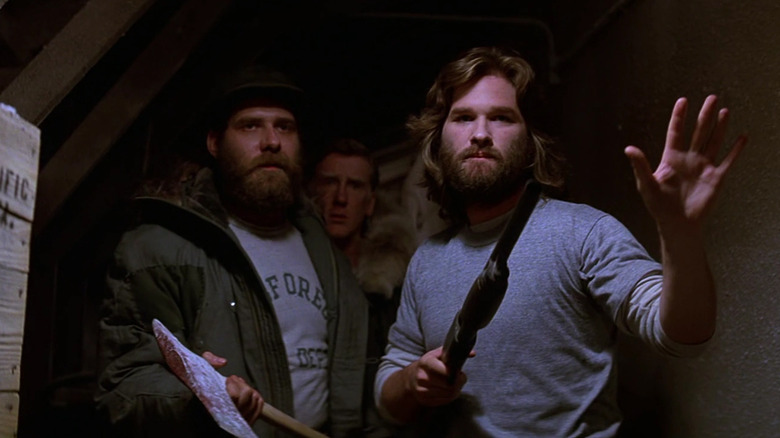 RJ MacReady (Kurt Russell) points a gun off-screen with his crew behind him in The Thing