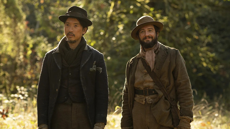 Orion Lee as King-Lu and John Magaro as Cookie, walking through a field in First Cow.
