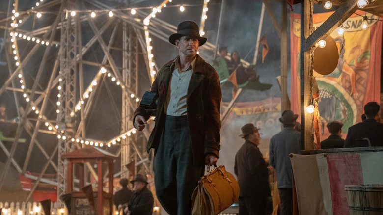 Bradley Cooper as Stanton Carlisle, walking through a carnival in Nightmare Alley.