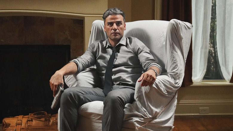 Oscar Isaac as William Tell, sitting in a covered chair and holding a gun in The Card Counter.