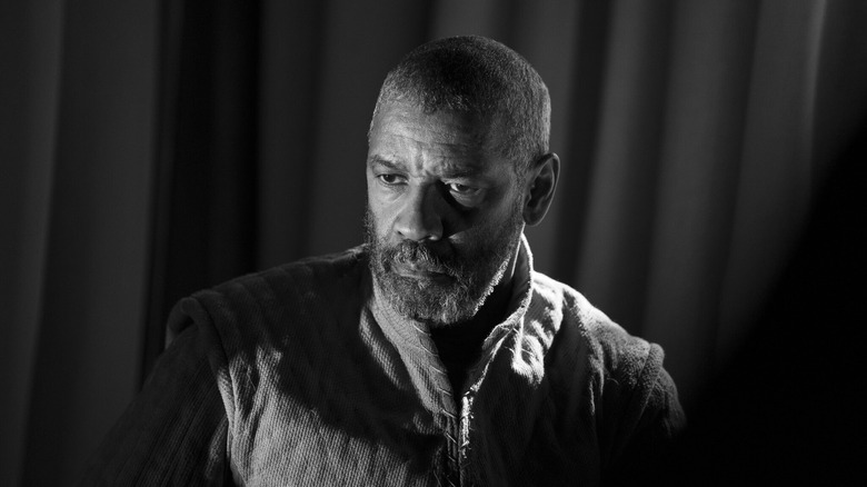 Denzel Washington as Macbeth, frowning and looking on in shadow in The Tragedy of Macbeth.