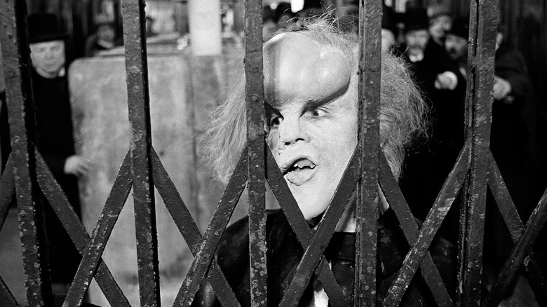 John Hurt as John Merrick looking through a gate in The Elephant Man