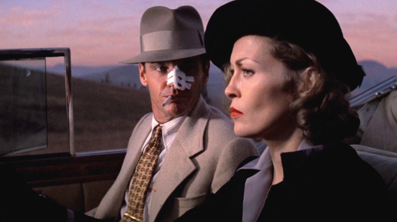Jack Nicholson as J. J. "Jake" Gittes and Faye Dunaway as Evelyn Cross-Mulwray in Chinatown, sitting in a car together as Gittes looks on at Evelyn with a bandage over his nose and cigarette in his mouth.